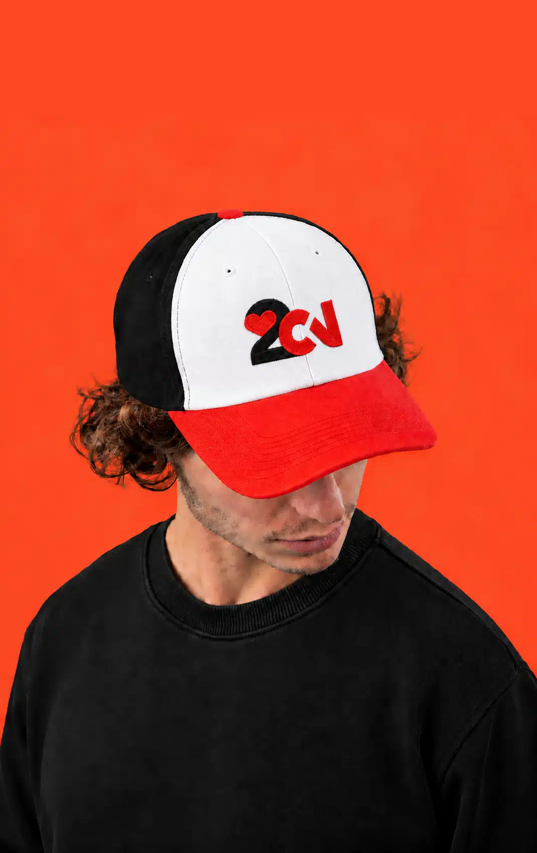 Person wearing a red, white and black cap with the 2CV logo against a red background